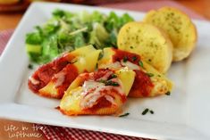 a white plate topped with stuffed shells covered in marinara sauce next to bread and veggies