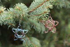 two ornament ornaments hanging from a pine tree's branch, one is made out of wire and the other is shaped like a star