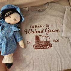 Step back in time and celebrate your love for simpler days with our "I Would Rather Be in Walnut Grove" t-shirt! Whether you're a fan of classic television, a lover of nostalgia, or someone who cherishes the warmth and community spirit of small-town life, this shirt is a perfect fit.  Crafted from soft, high-quality cotton, it's not just a statement piece, but also incredibly comfortable for everyday wear. The vintage-inspired design adds a touch of rustic charm, making it a great gift for fans of timeless shows or anyone who dreams of escaping to a peaceful, idyllic place like Walnut Grove. Wear it to share your love for this iconic setting or to remind yourself that sometimes, the best moments are found in the simplicity of country life. Order yours today and wear your love for Walnut Gr Vintage Cotton T-shirt As Gift, Timeless Show, Walnut Grove, Small Town Life, I Would Rather, Classic Television, Charm Making, Step Back, Vintage Inspired Design