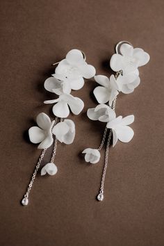 three white flowers with chains attached to them on a brown tablecloth, one is dangling from the chain