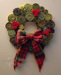 a christmas wreath made out of buttons with a red bow hanging on the wall next to it