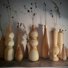 several wooden vases are lined up on a shelf with dried flowers in the middle