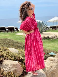 a woman standing on top of a rock next to the ocean wearing a pink dress