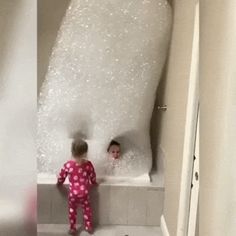 two children are in the bathtub and one is looking at the bubbles on the wall