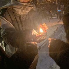 two people holding a lit candle in their hands while standing on the snow covered ground