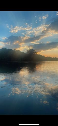 the sun is setting over a lake with trees in the distance and clouds reflected in the water