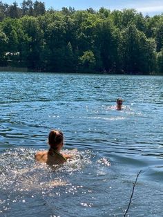 two people swimming in the water near some trees