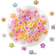 a white plate topped with lots of different colored beads next to small pink and yellow flowers