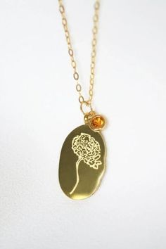 a gold necklace with a pendant that has a tree on it and a small yellow bead