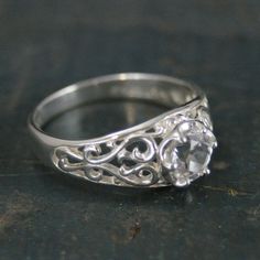 a white gold ring with an intricate filigree design and a round diamond in the center