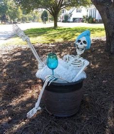 a skeleton in a tub with two wine glasses sitting on the ground next to a tree