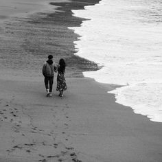 two people walking on the beach with footprints in the sand