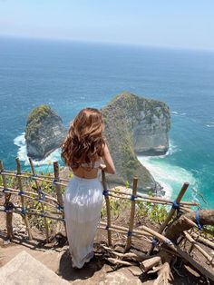 a woman standing at the top of stairs looking out over the ocean and cliffs in the distance