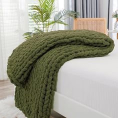 a green blanket on top of a bed next to a chair and potted plant