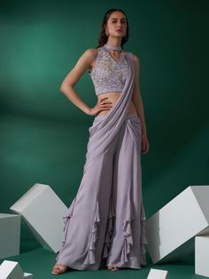 This is a two-piece lilac pre draped pant saree set from the Suruchi Parakh collection. The lilac pre draped pant saree is paired with a hand-embroidered cutout blouse. The sleeveless blouse has heavy floral sequin-pearl-bead work. The cutout blouse has padding and a back hook cutout opening. The pre draped saree has a drape style attached to the palazzo flare pants with ruffle flare at the hem. This lilac pre draped pant saree set is crafted in georgette crepe and satin materials. Modern Saree With Pants, Drape Saree With Pants, Drape Saree Indo Western, Saree With Pants, Engagement Party Attire, Pant Saree, Hand Embroidered Blouse, Fancy Shirt, Lehenga Designs Simple