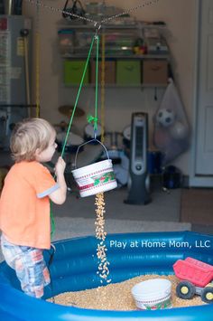 a little boy playing in an inflatable pool with a bucket full of sand