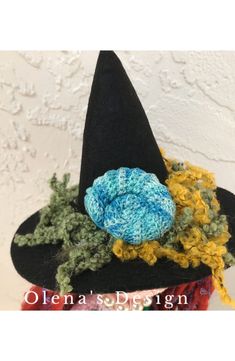 a crocheted witches hat with a blue flower on the front and yellow yarn in the center