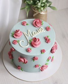 a blue cake with pink roses and the word maue on it is next to a potted plant