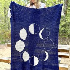 a woman holding up a blue crocheted blanket with white circles and tassels