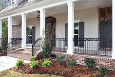 a white house with black iron railings on the front porch and side entry door