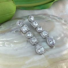 three pairs of diamond earrings sitting on top of a white rock next to a green plant