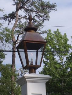 an old fashioned street light on top of a white pillar in front of some trees