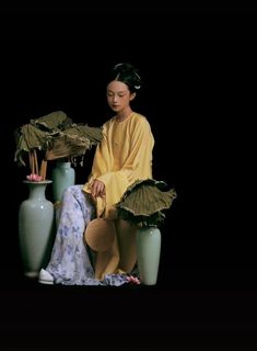 a woman sitting next to two vases with flowers in them