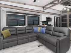 a large sectional couch in the middle of a living room with two windows and a ceiling fan