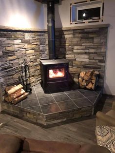 a living room with a fire place in the middle of it and wood logs on the floor