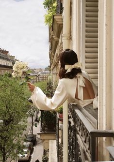 a woman in a white dress holding a bouquet of flowers on the balcony of a building