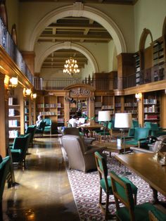 the large library is full of books and chairs with green upholstered seats on either side