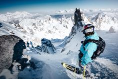 a person on skis standing at the top of a snow covered mountain with mountains in the background