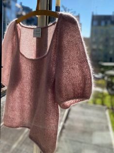 a pink sweater hanging on a clothes line in front of a window with cityscape