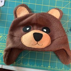 a brown teddy bear hat sitting on top of a cutting board next to a ruler