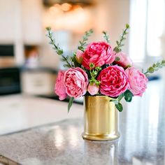 pink flowers are in a gold vase on the counter