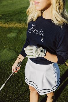 a woman holding a golf club and wearing a shirt with the word bride on it