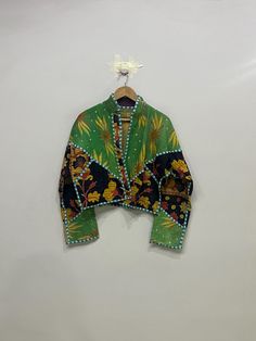 a green jacket hanging on a wall with a white flower in the center and an orange, yellow, and blue design on it