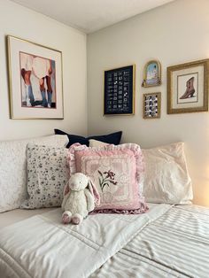 a white bed topped with lots of pillows next to pictures on the wall above it