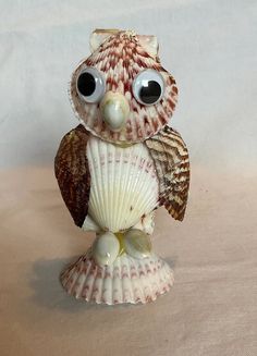 an owl figurine sitting on top of a seashell with large black eyes