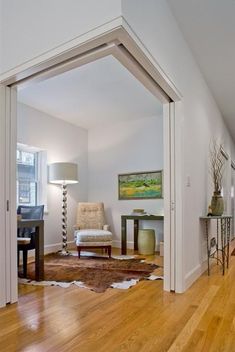 an open door leading to a living room with hardwood floors and white walls, along with a painting on the wall