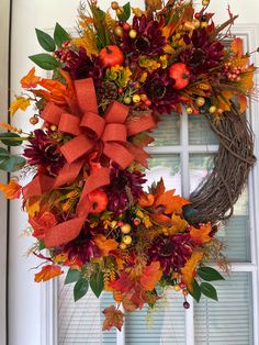 a wreath with orange and red flowers is hanging on the front door window sill