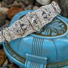 This elegant circa 1920s link bracelet is centered with a row of three (3), bead set, old European cut diamonds. The bracelet is also accented with one hundred sixty (160), bead set, old European/single cut diamonds, two (2), bezel set, cabochon cut synthetic sapphires and twenty (20), bezel set, calibre' cut synthetic sapphires. The gemstones are bordered with milgrain edging. The bracelet measures 18.4mm wide at the center and tapers to 5.0mm wide at the clasp. The bracelet measures 8-1/4 inches in length and finished with a hidden box clasp and safety chain. Vintage Diamond Bracelet With Hand-set Diamonds, Vintage Hand Set Diamond Bracelet, Formal Art Deco Diamond Tennis Bracelet, Vintage Platinum Diamond Bracelet With Single Cut Diamonds, Art Deco Diamond Tennis Bracelet For Anniversary, Vintage Diamond Tennis Bracelet With Single Cut Diamonds, Diamond Art Deco Tennis Bracelet For Anniversary, Art Deco Tennis Bracelet With Diamond Accents For Anniversary, Vintage Diamond Bracelet For Anniversary