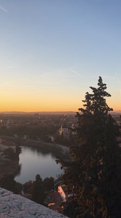 the sun is setting over a lake and cityscape with trees in the foreground