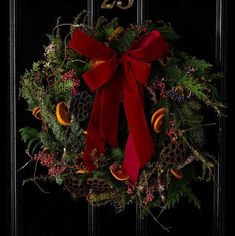 a christmas wreath with red bow hanging on the front door number twenty five, decorated with pine cones and berries