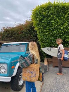 two people standing in front of a blue truck with a surfboard on the back