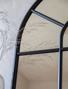 a vase with some flowers in it next to a window that has an arched glass