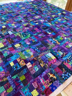 a quilt made with many different colors and patterns on the table top, next to a window