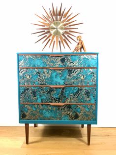 a blue and gold dresser sitting on top of a wooden floor next to a clock