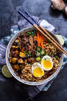 a bowl filled with noodles, meat and vegetables next to chopsticks on a table