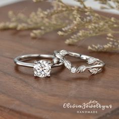 two wedding rings with leaves on them sitting on top of a wooden table next to flowers